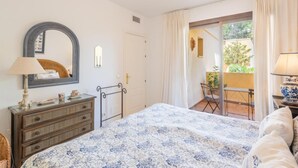 Ein Schlafzimmer mit Bett, Kommode, Spiegel und Blick auf eine Terrasse.
