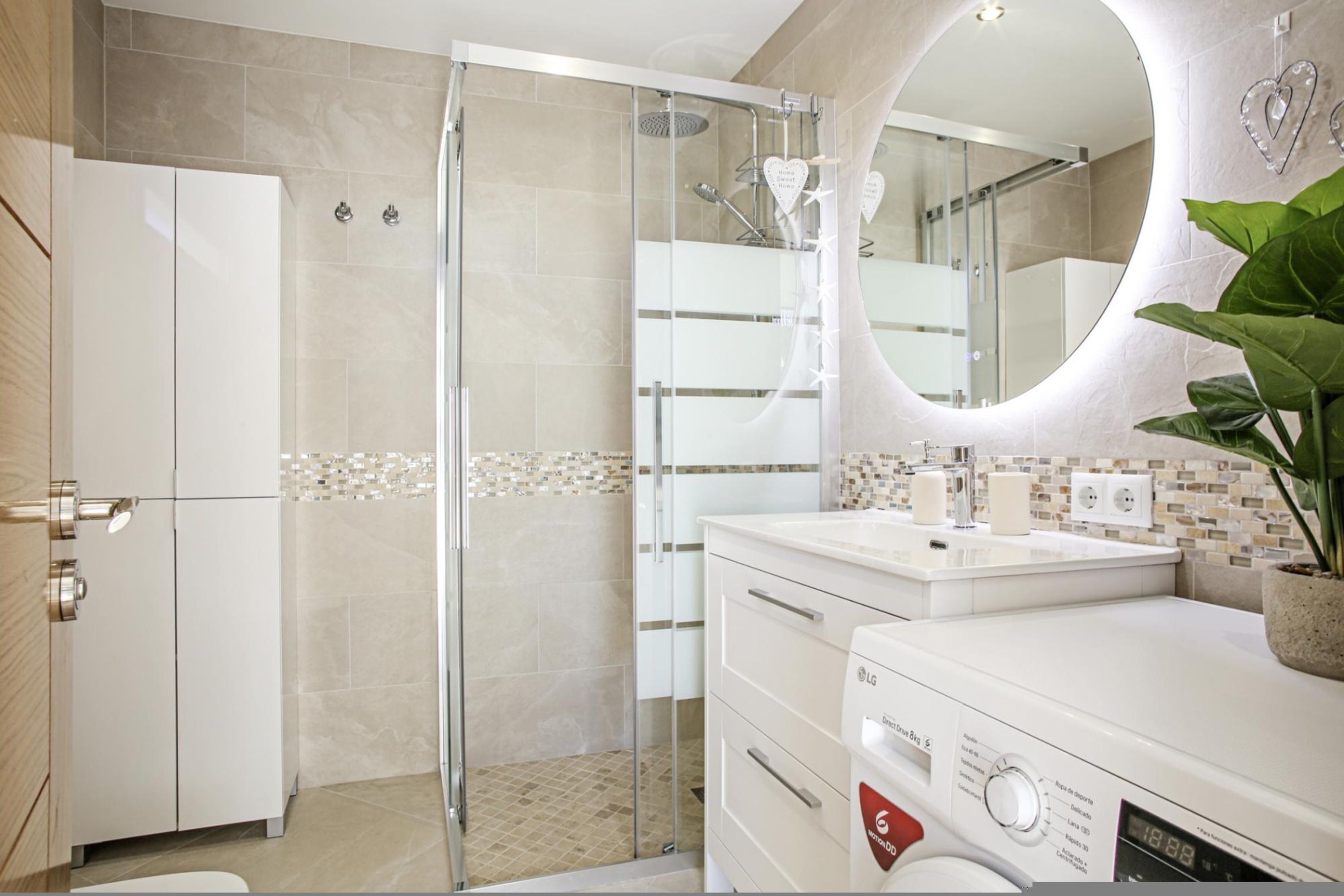 A modern bathroom with a glass shower enclosure, a white sink with a mirror, and a built-in washing machine.