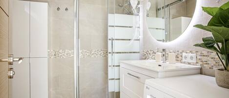 A modern bathroom with a glass shower enclosure, a white sink with a mirror, and a built-in washing machine.