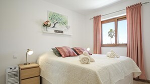 A bedroom with a bed, a nightstand, a heater, a window with curtains, and a wall-mounted picture. - Sand Club Apartment 202 (San Miguel de Abona)