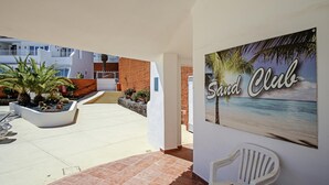 A courtyard with a view of a beach, a sign reading "Sand Club", and a white chair. - Sand Club Apartment 202 (San Miguel de Abona)