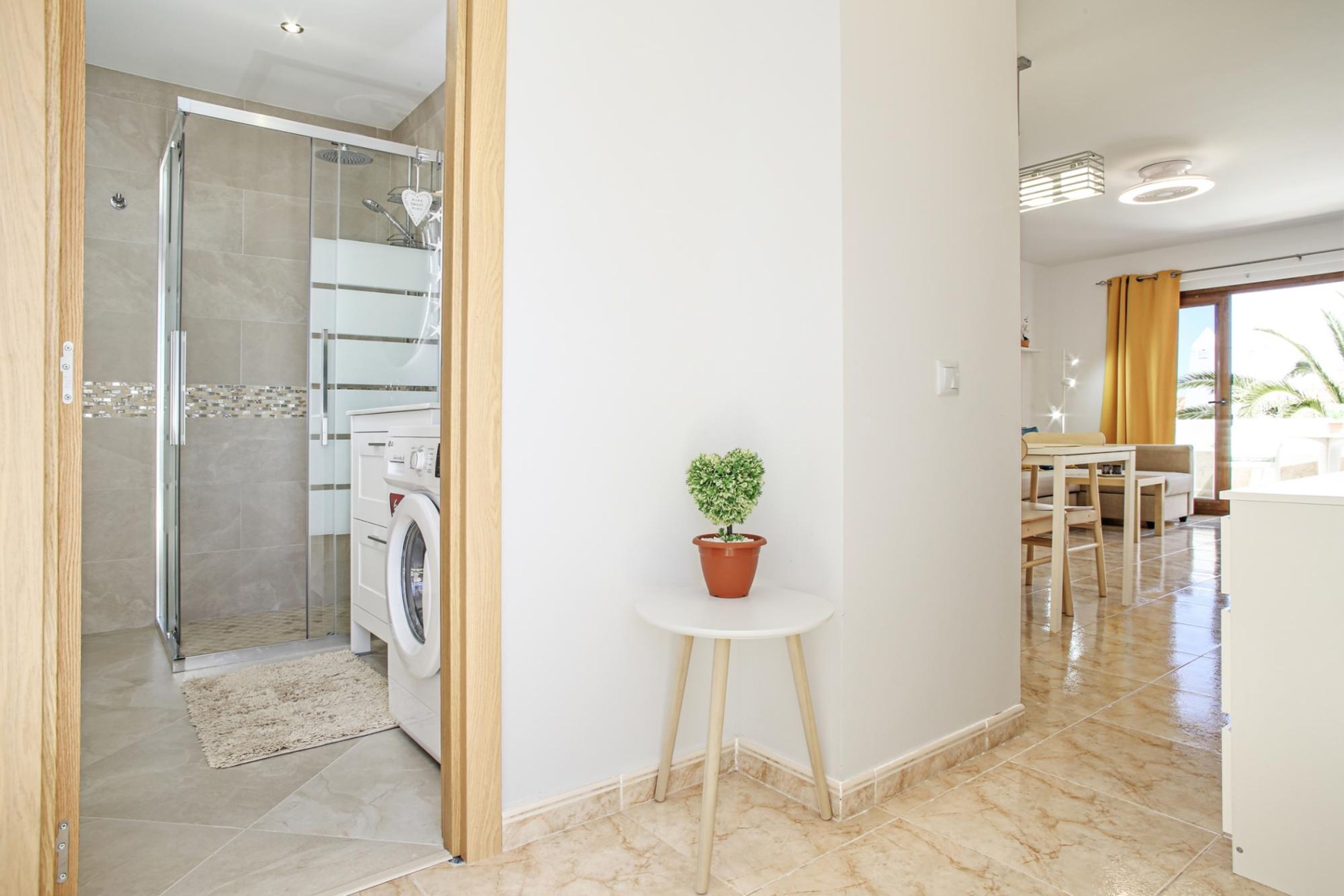 A modern bathroom with a glass shower enclosure, a washing machine, and a small table with a potted plant.