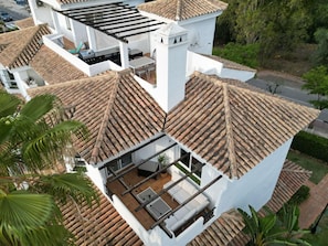 A modern house with a tiled roof, a balcony with a white railing, and a patio area with a table and chairs.