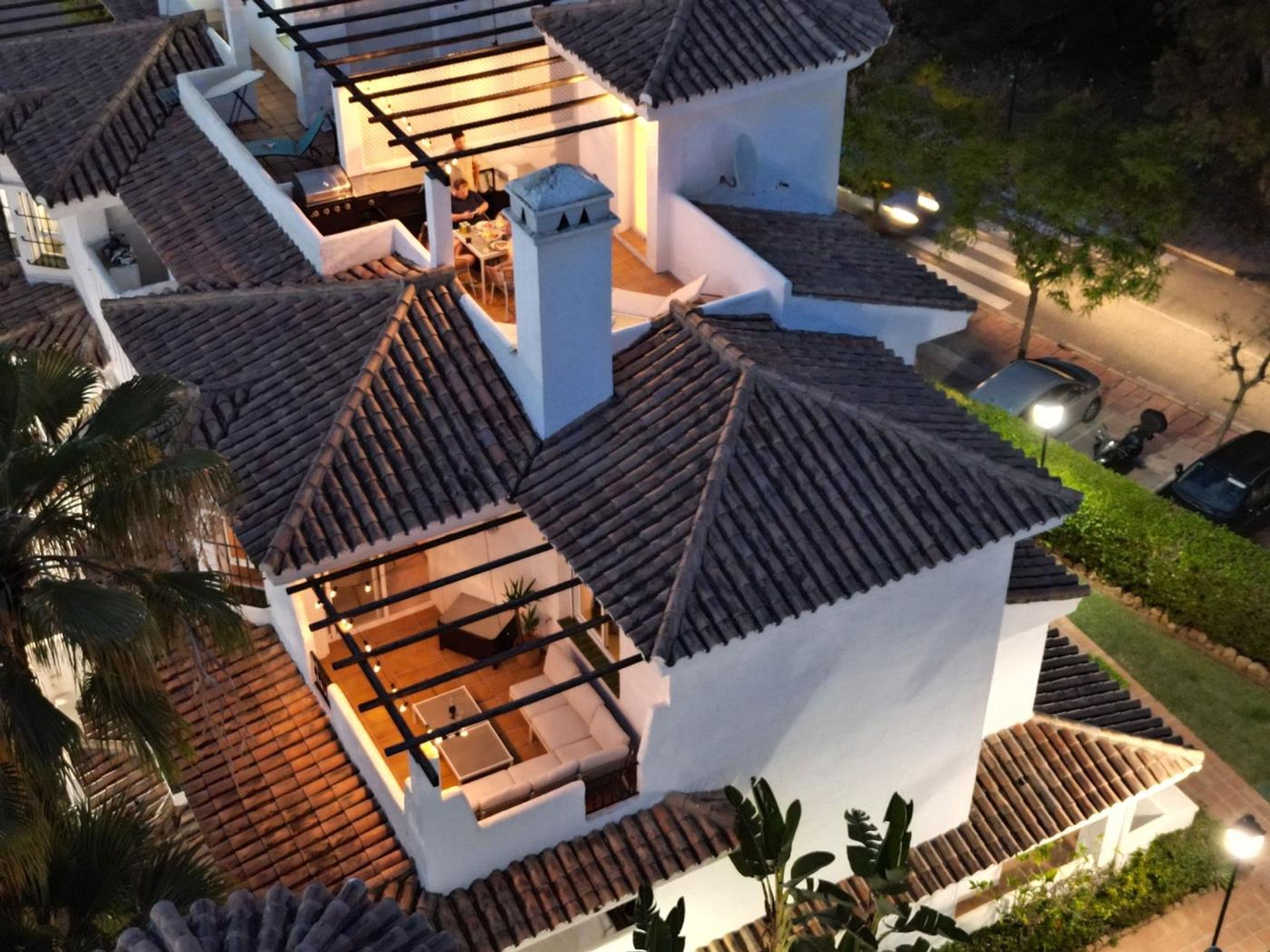 Una casa de varios niveles con techo de tejas, un patio con mobiliario exterior y vista a la calle.