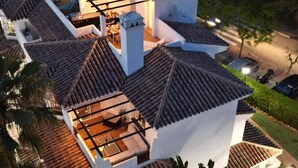 Una casa de varios niveles con techo de tejas, un patio con mobiliario exterior y vista a la calle.