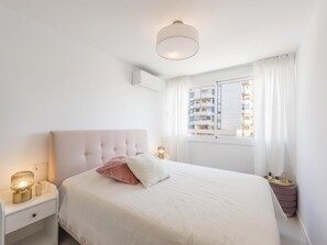 A bedroom with a bed, nightstand, bedside lamp, window with curtains, and a view of buildings. - Front Line Beach in Marbella (Marbella)