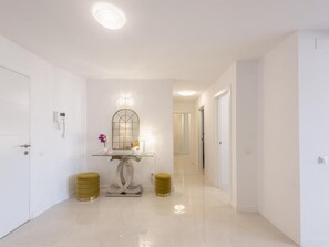 A hallway with a glass console table, two gold stools, a mirror, and a door with a phone on the wall. - Front Line Beach in Marbella (Marbella)