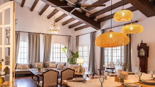 A dining area with a wooden table set for a meal, a sofa in the background, and a ceiling fan. - Charming Villa Domingo Playa Portaventura Golf (Cambrils)
