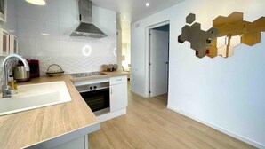 A modern kitchen with white cabinets, a stainless steel range hood, a wooden countertop, and a unique hexagonal wall decoration. - Precioso Tico Cerca de la Playa y Port Aventura (Salou)