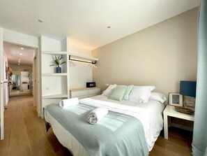 Ein modernes Hotelzimmer mit einem ordentlich bezogenen Bett, einem Nachttisch mit Lampe, einem kleinen Nachttisch mit Dekoration und einem Wandregal mit Pflanze.