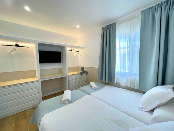 Ein Hotelzimmer mit Bett, Wandfernseher, Ventilator und einem Fenster mit Vorhängen.