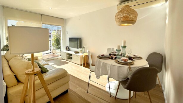 A modern living room with a dining area, a sofa, a TV, and a large window. - Precioso Tico Cerca de la Playa y Port Aventura (Salou)