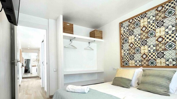 A bedroom with a bed, pillows, a wall-mounted shelf with baskets, and a patterned tile wall. - Fabuloso Apartamento Cerca Playa y Portaventura (Salou)