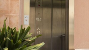 An elevator with a control panel, a warning sign, and a plant in the foreground. - Fabuloso Apartamento Cerca Playa y Portaventura (Salou)