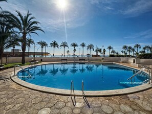 A large, clear swimming pool with palm trees and a view of the ocean. - Apartamento N Utico (Alicante)
