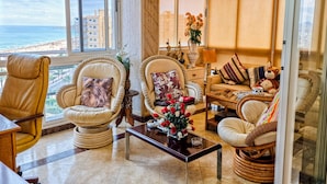 A spacious living room with a view of the beach, featuring comfortable seating, a coffee table, and decorative items. - Apartamento N Utico (Alicante)