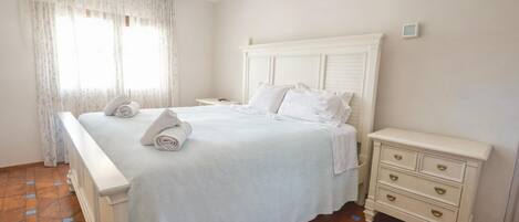 Quarto de hotel com uma cama grande, mesa de cabeceira e janela com cortinas.
