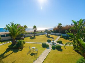 A well-maintained garden with a fountain, palm trees, and a view of the sea. - Villa Drita in Estepona (Estepona)