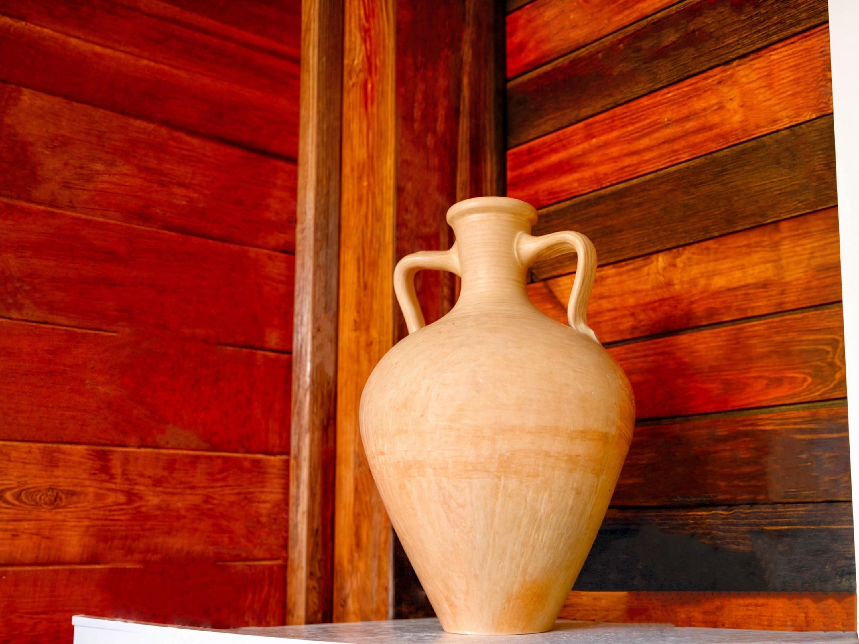 A ceramic vase with two handles on a white surface against a wooden background.