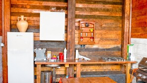 A compact kitchen with wooden walls, a white refrigerator, a sink, a stove, and a shelf with kitchenware. - Casa Stardust in El Palmar- Vejer de la Frontera (Vejer de la Frontera)