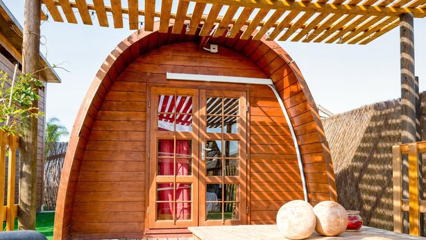 A wooden cabin with a curved roof, a wooden door with glass panels, and a small outdoor seating area with a table and chairs. - Casa Stardust in El Palmar- Vejer de la Frontera (Vejer de la Frontera)