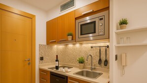 Una cucina compatta con mobili in legno, un forno a microonde in acciaio inossidabile, una lavastoviglie, un lavello e una pianta in vaso.