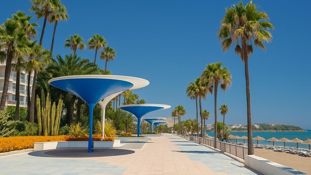 Passeggiata con palme e ombrelloni blu lungo il lungomare.