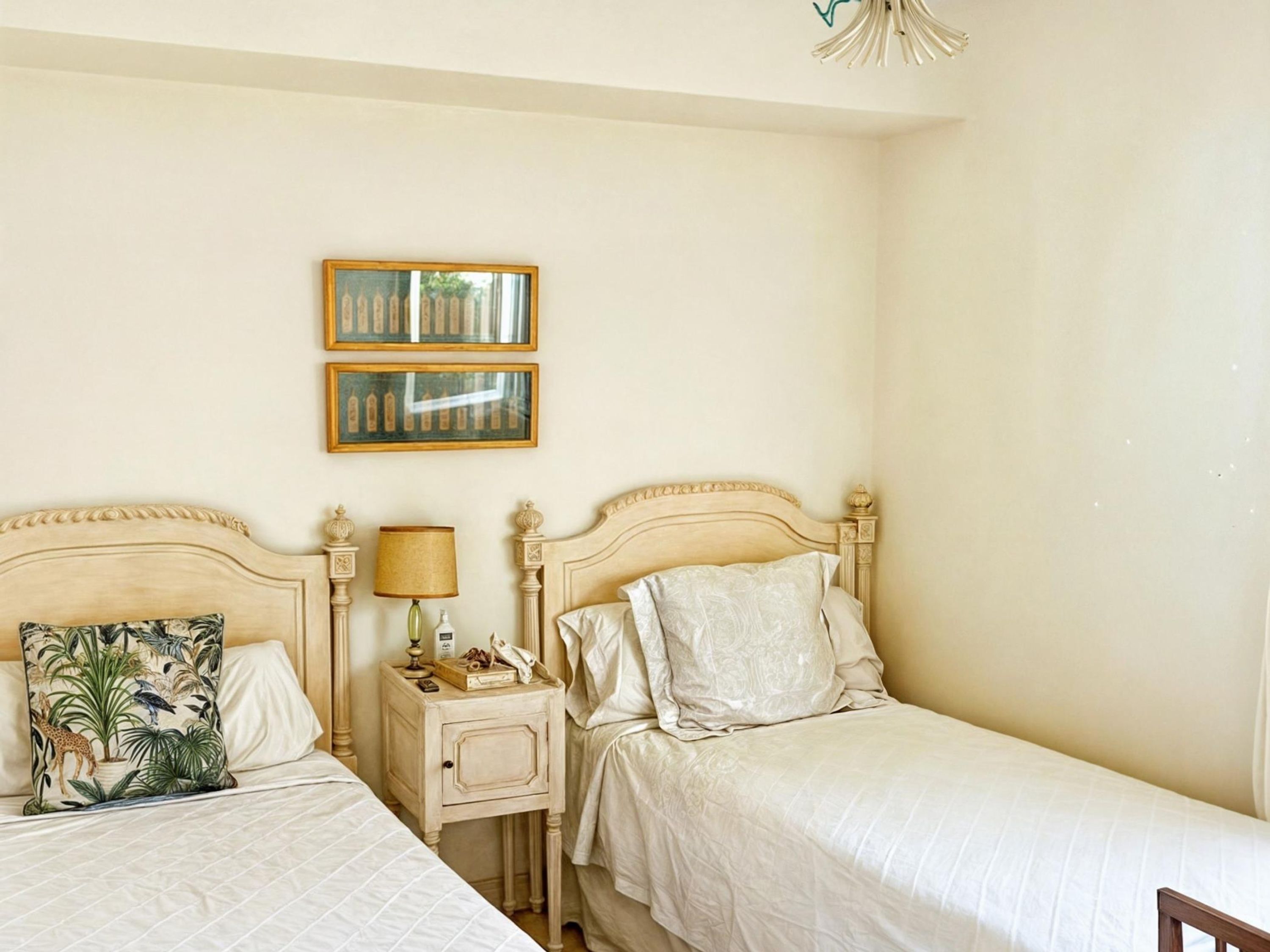 A hotel room with two beds, a nightstand with a lamp, a telephone, and framed pictures on the wall.