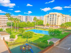 Um complexo residencial com piscina, parquinho e palmeiras.