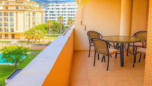 A balcony with a table and chairs, overlooking a pool and buildings. - Apartamento Parque Central (Estepona)