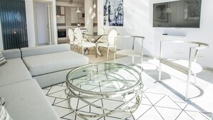 A modern living room with a glass coffee table, a sofa, and a dining area with chairs.