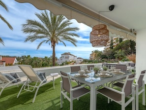 An outdoor dining area with a glass table, white chairs, and a view of palm trees and buildings.