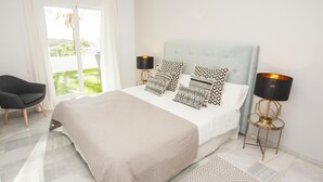 A bedroom with a large bed, two bedside lamps, a chair, and a view of the outdoors.
