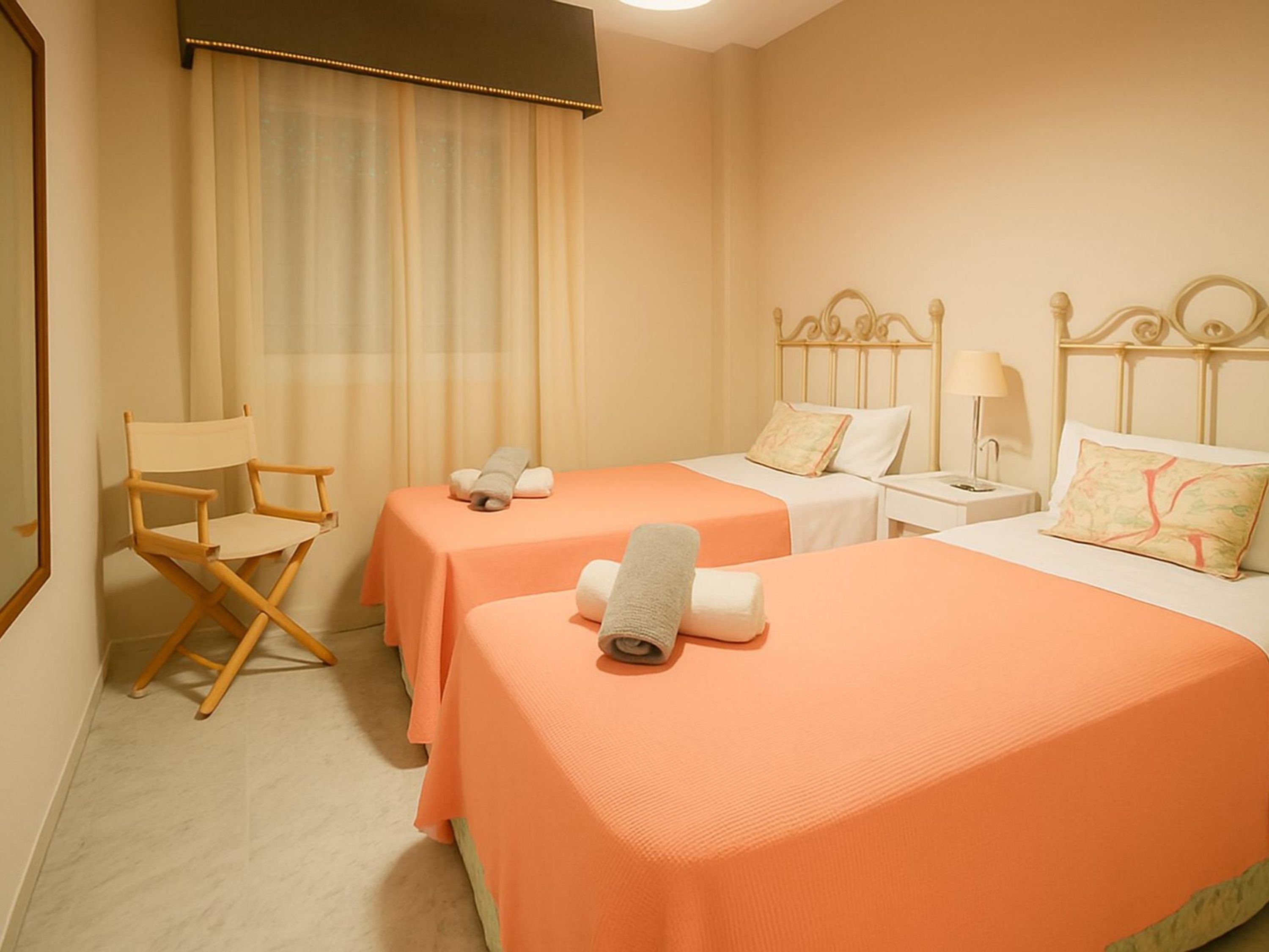 A hotel room with two beds, a chair, a nightstand, and a window with curtains.