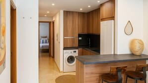 Une cuisine moderne avec des meubles en bois, un lave-linge encastré, un évier et un coin bar avec deux tabourets.