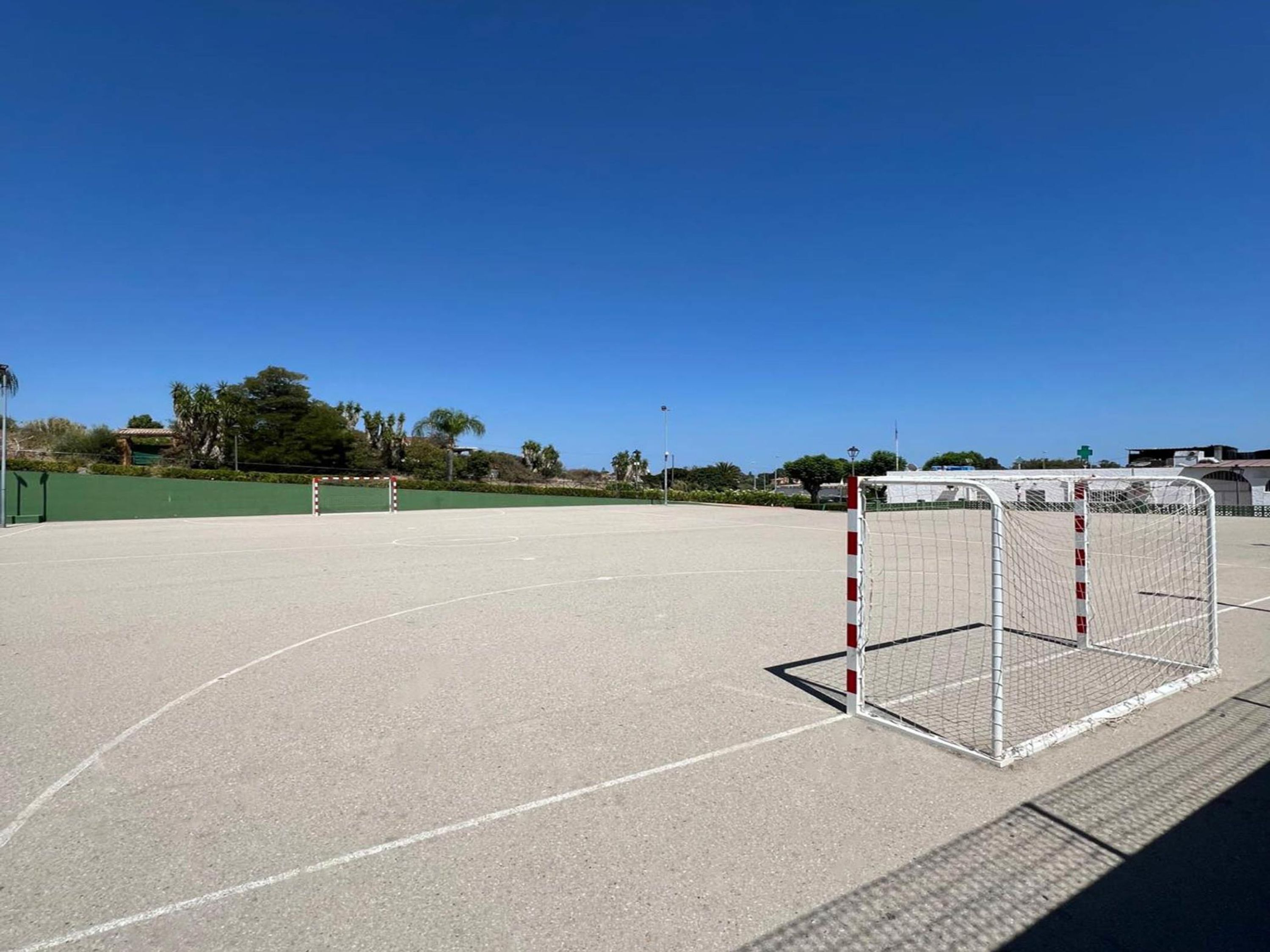 Ein Sportplatz im Freien mit einem Tor, blauem Himmel und einem grünen Zaun im Hintergrund.