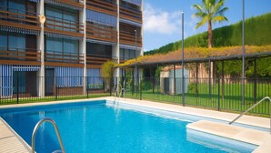 A swimming pool with a clear blue water, surrounded by a metal fence and a wooden deck. - Apartamento Para so Ban s (Marbella)