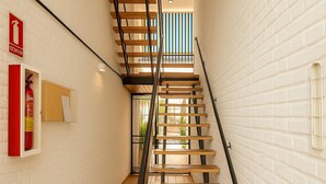 A narrow stairwell with wooden steps and black railings, white brick walls, a fire extinguisher, and a bulletin board. - Apartamento Para so Ban s (Marbella)