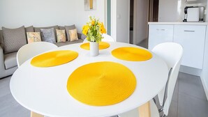 A modern living room with a white round table, yellow placemats, a sofa with patterned cushions, and a vase with flowers. - Apartamento Para so Ban s (Marbella)