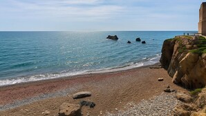 A coastal beach with a rocky cliff and a building on the right. - Apartamento Do a Lucia Resort (Estepona)