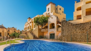 Ein Schwimmbecken, umgeben von Gebäuden im mediterranen Stil, darunter gewölbte Fenster und Steinmauern.