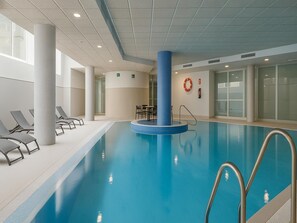 An indoor swimming pool with clear water, surrounded by lounge chairs and a central column.