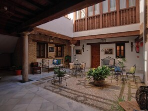 Un patio con zona de estar cubierta, pared de ladrillo y balcón de madera.