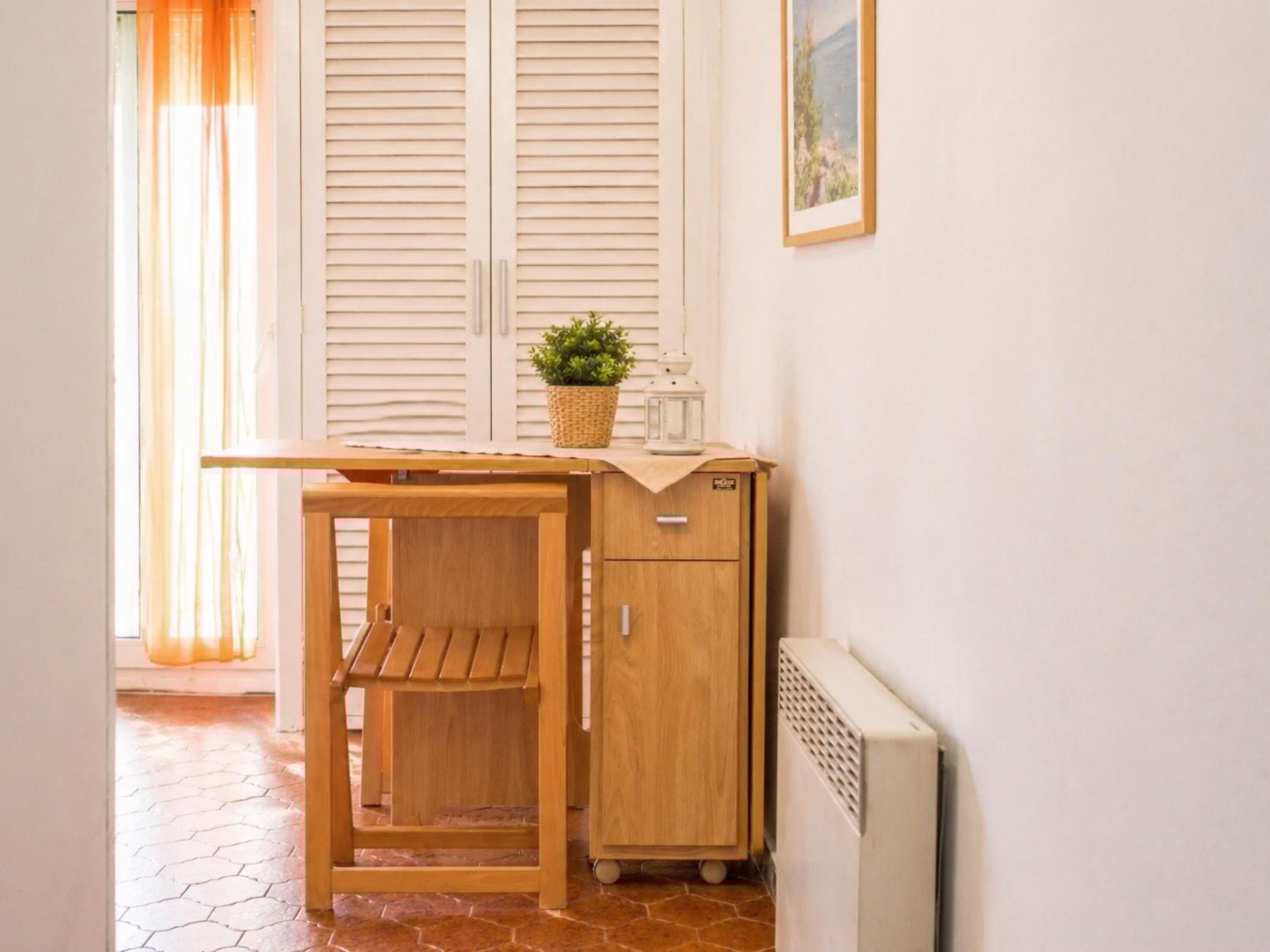 Una habitación pequeña con un escritorio de madera, un mueble bajo, un radiador y una planta en maceta.