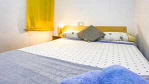 Ein Einzelbett mit einem gemusterten Überwurf, einem grauen Kopfkissen und einem gelben Vorhang.