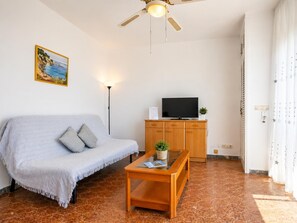 Een woonkamer met een bank, een salontafel, een televisie op een houten kast, een plafondventilator en een schilderij aan de muur.
