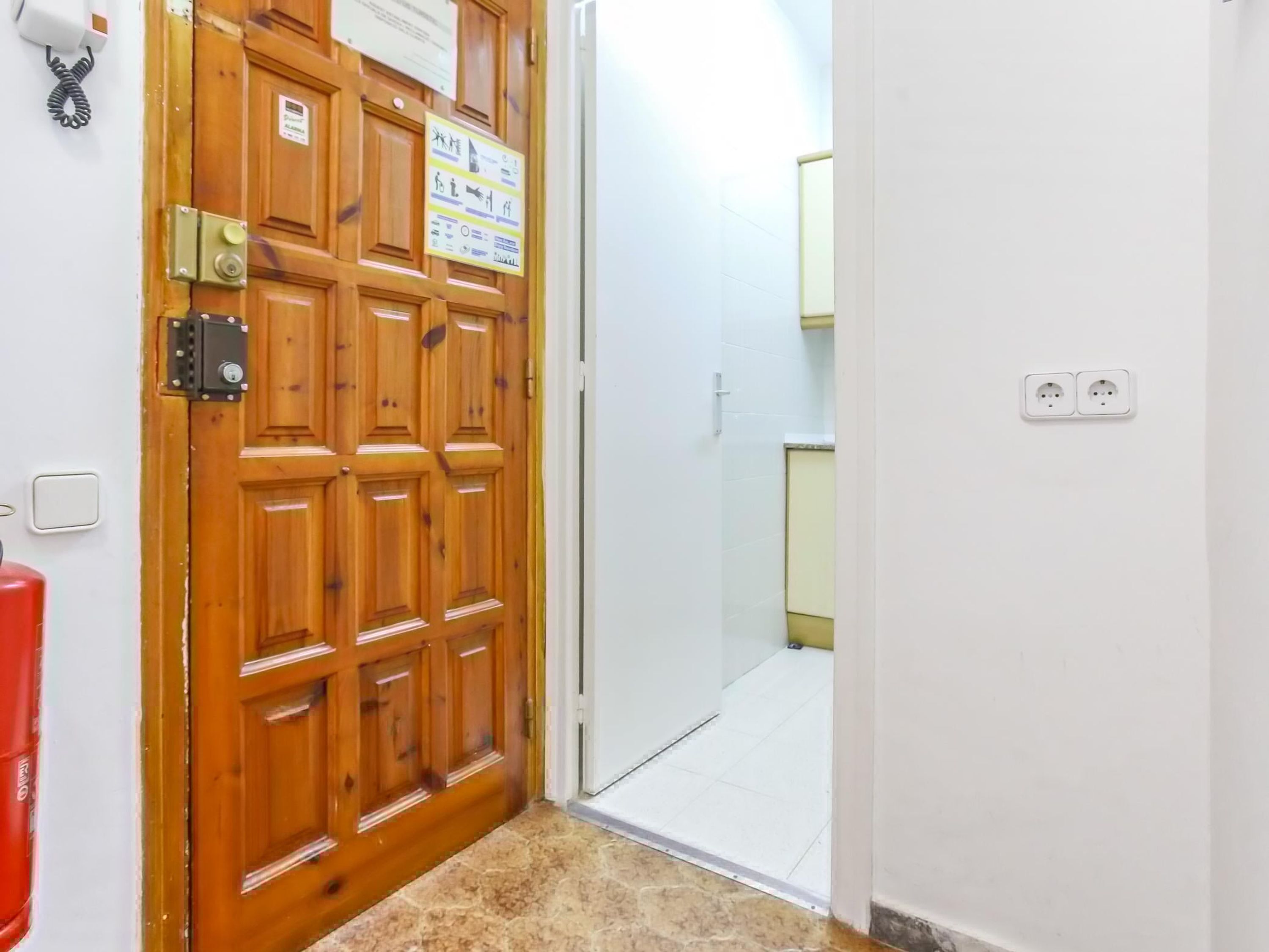 Una puerta de madera con un cartel, un interruptor de luz y un extintor.