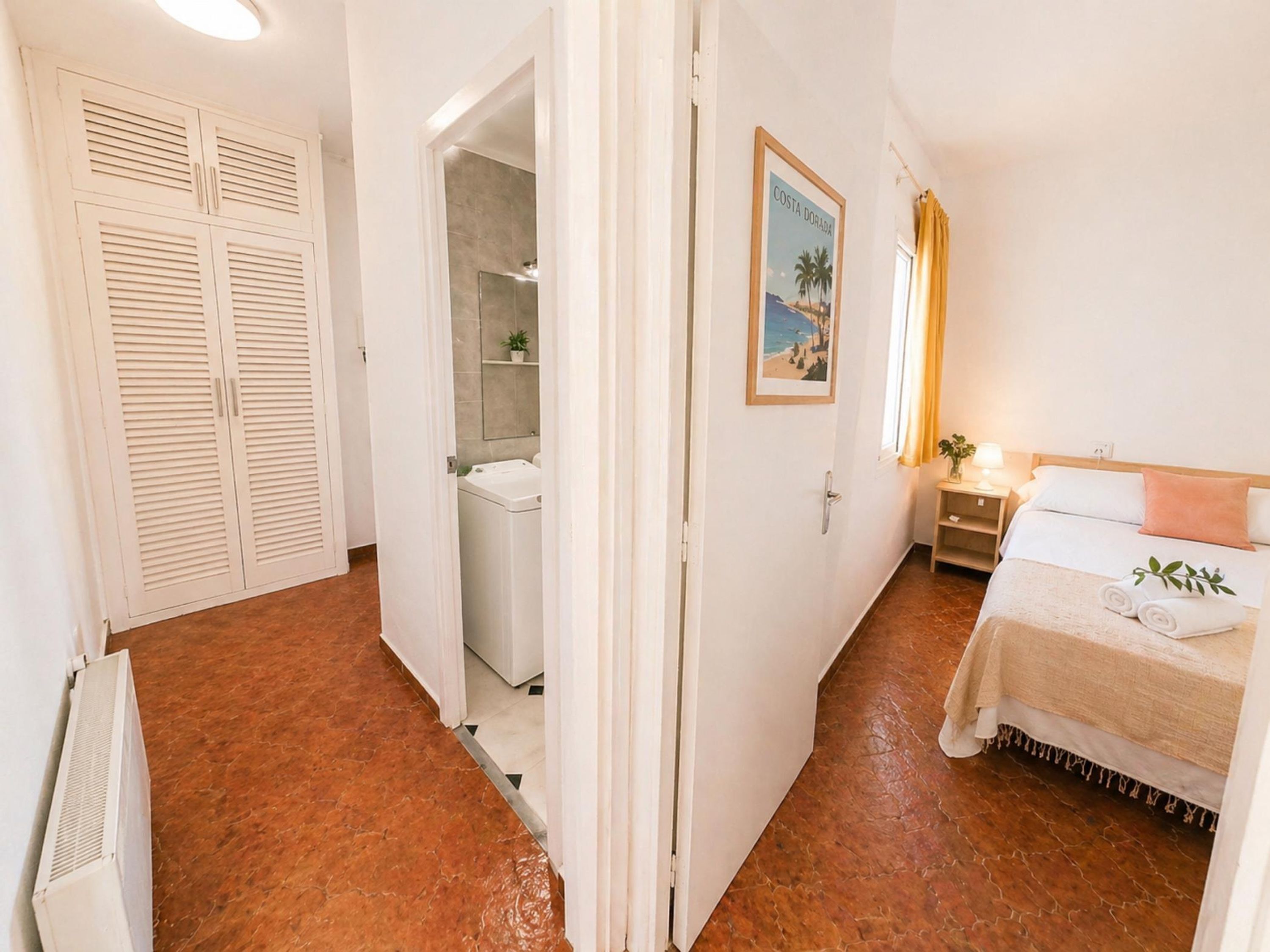 Habitación de hotel con cama, mesita de noche, un cuadro en la pared y un baño visible a través de una puerta abierta.