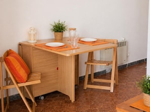 Een gezellig eetgedeelte met een houten tafel, twee stoelen, een kleine plant in pot, een glazen pot en een wit bord.