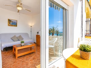 A room with a sofa, a wooden coffee table, a ceiling fan, and a view of the sea through a glass door. - Apartamento Acogedor en Primera Linea Liliane (Sitges)
